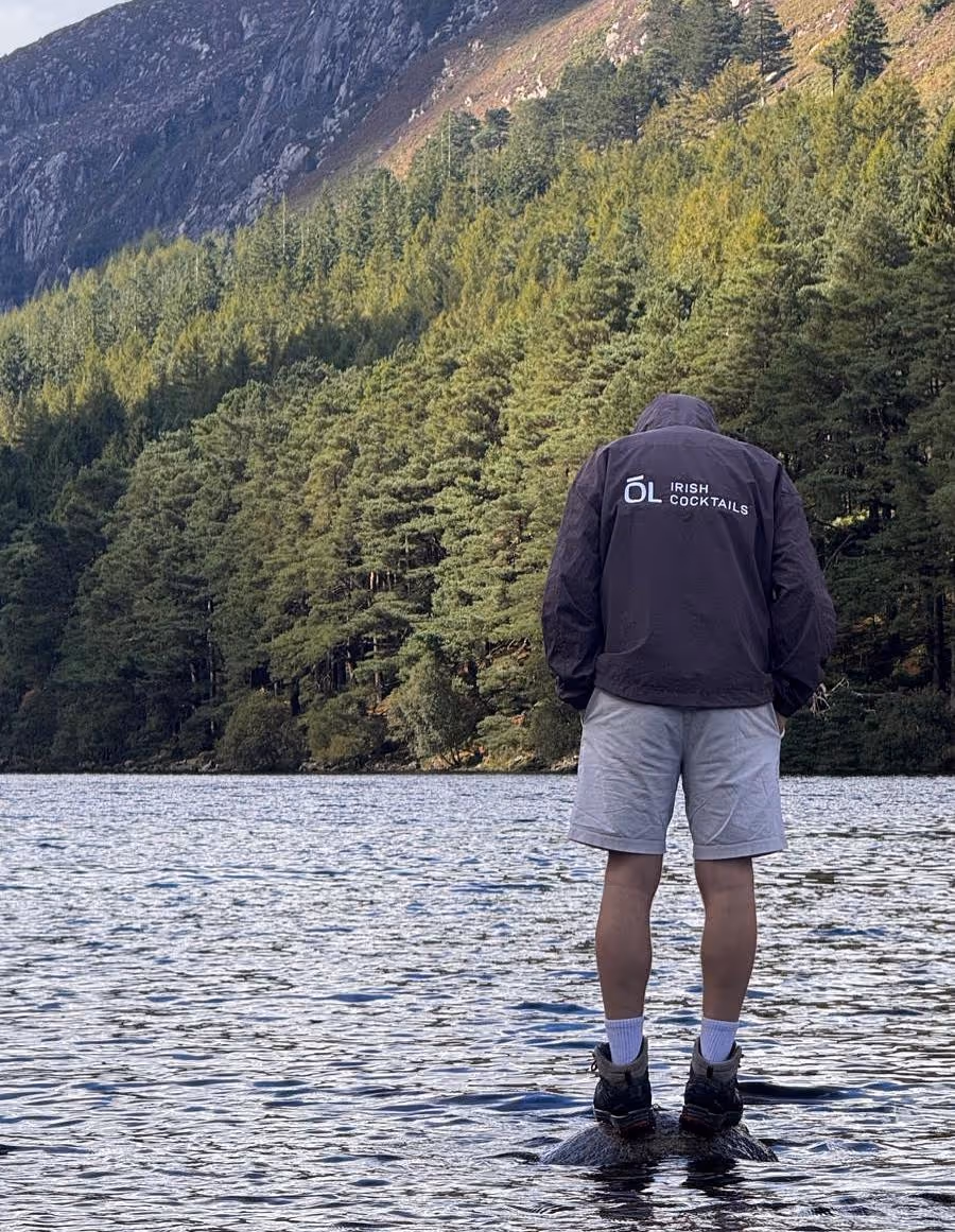 Man standing on a stone in a lake with an Ól Irish Cocktails hoodie